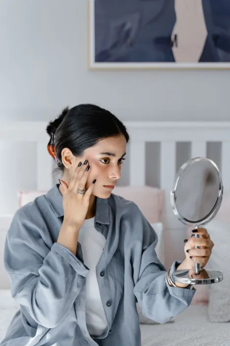 Woman worried about her skin, touching her face in a hand mirror