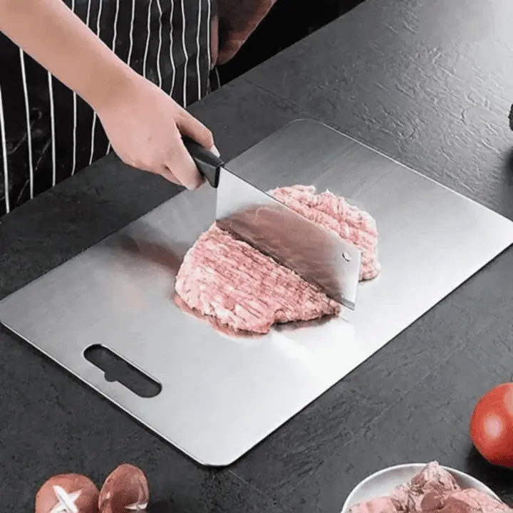 Raw minced meat being cut with a cleaver on a flat metal cutting board with a handle cut-out