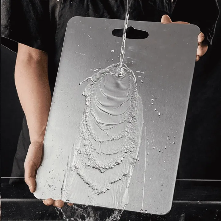 Water poured onto the smooth brushed surface of a metal cutting board held over a sink