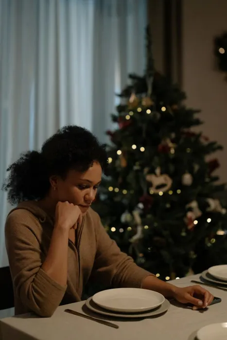 Woman sitting alone at a Christmas dinner table next to the tree